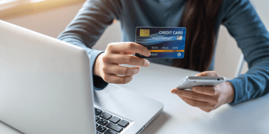 Hand håller bankkort framför datorskärm, symbol för bankbedrägeri efter bluffsamtal från falsk bankman.